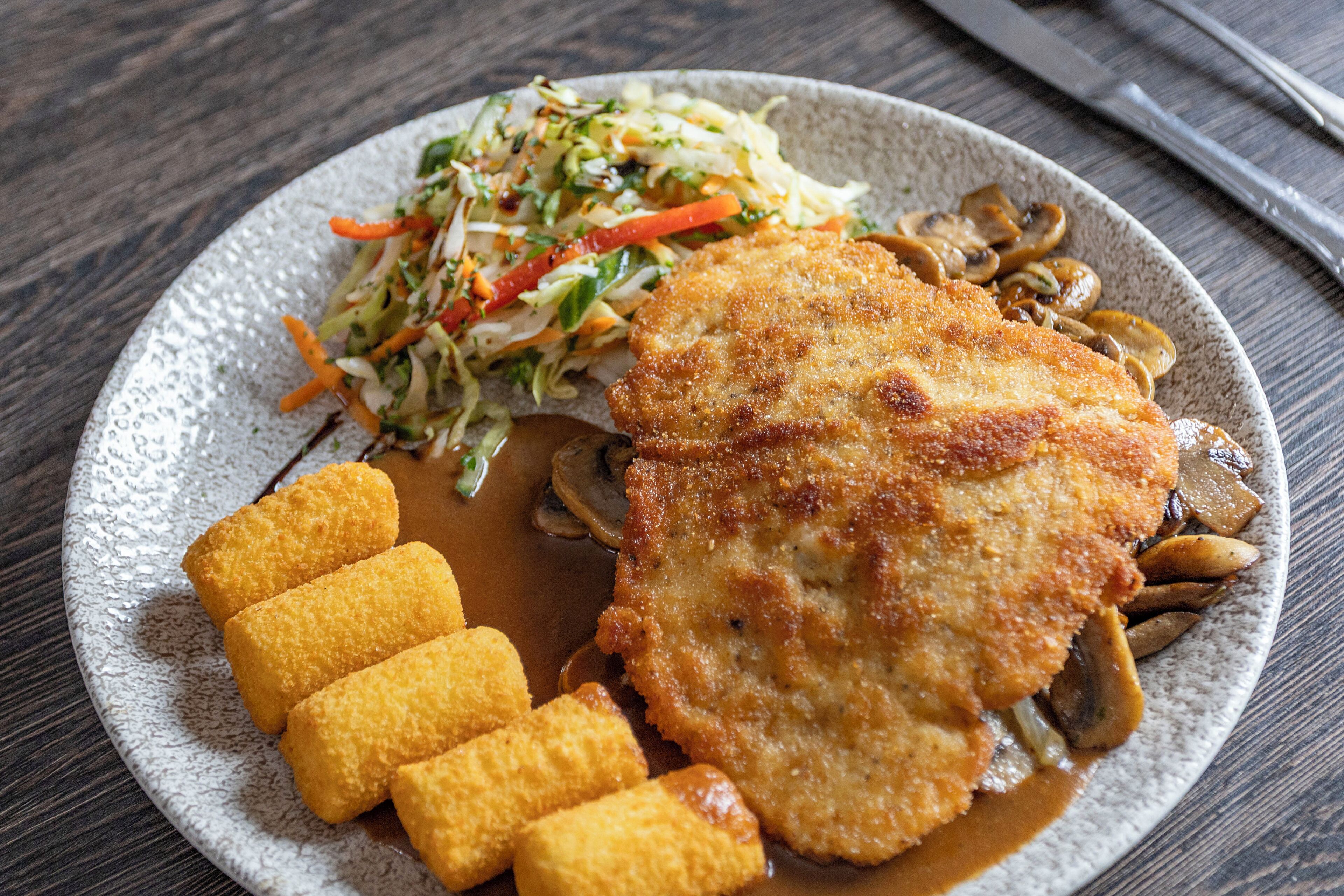 Une assiette comprenant une escalope panée, des champignons et une salade en accompagnement.