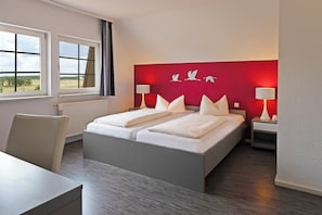 A hotel room with a large bed, two bedside tables, a chair, and a view of the outdoors through two windows. - Hotel ElbRivera Magdeburg (Magdeburg)