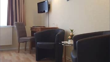 A living room with a sofa, a chair, a small table with a vase, and a television mounted on the wall.