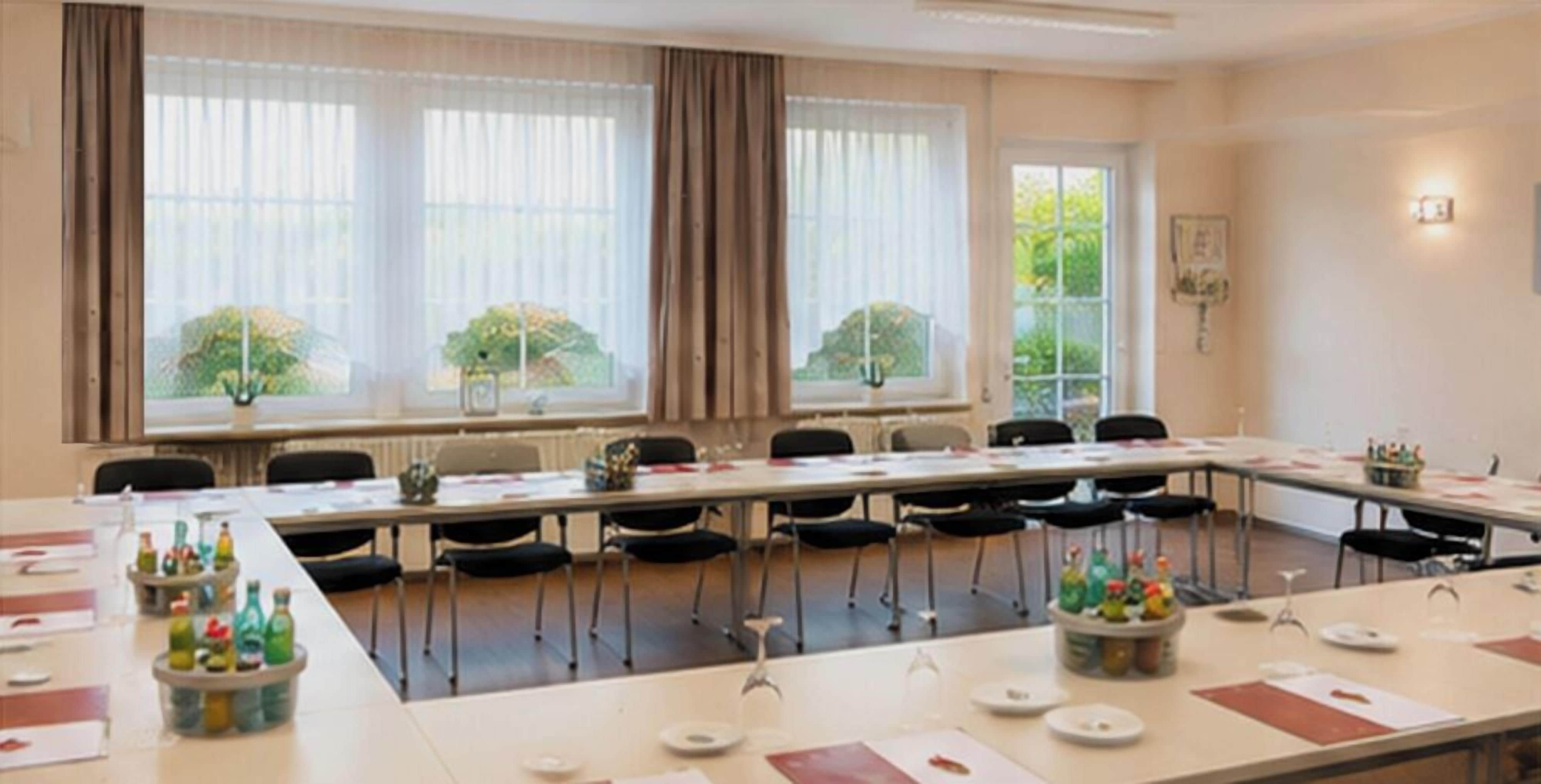 Ein Konferenzraum mit einem langen Tisch, Stühlen und einem Fenster mit Vorhängen.