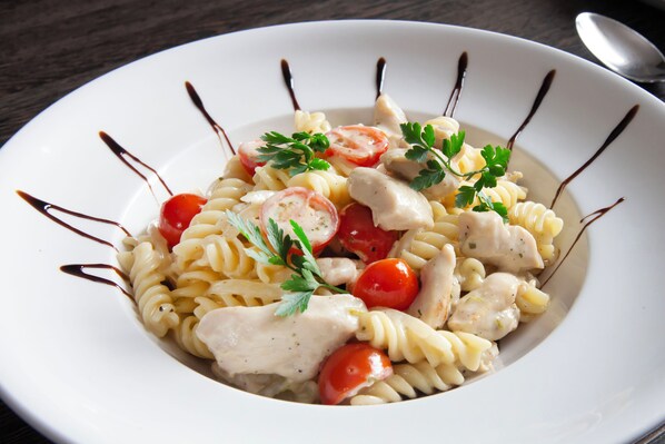 A white plate with pasta, cherry tomatoes, and chicken, garnished with parsley.