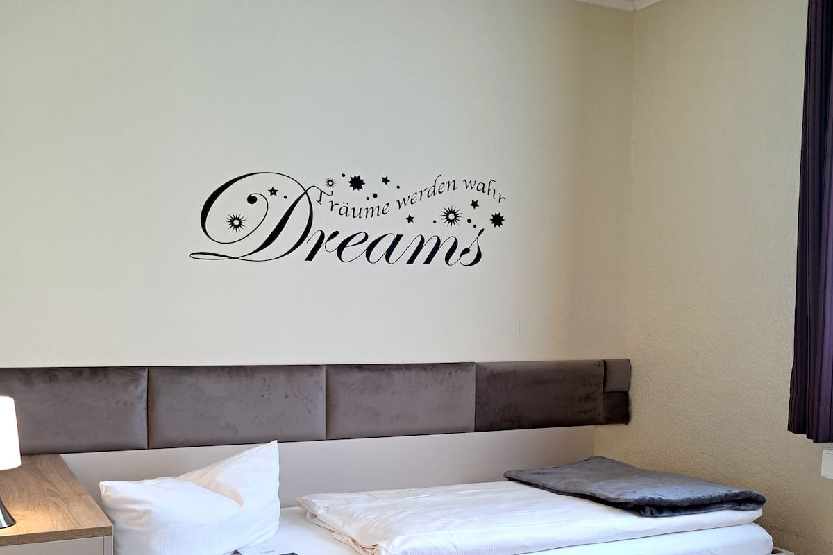 A neatly made bed with a headboard, a bedside table with a lamp, and a wall decoration with the text "Dreams".