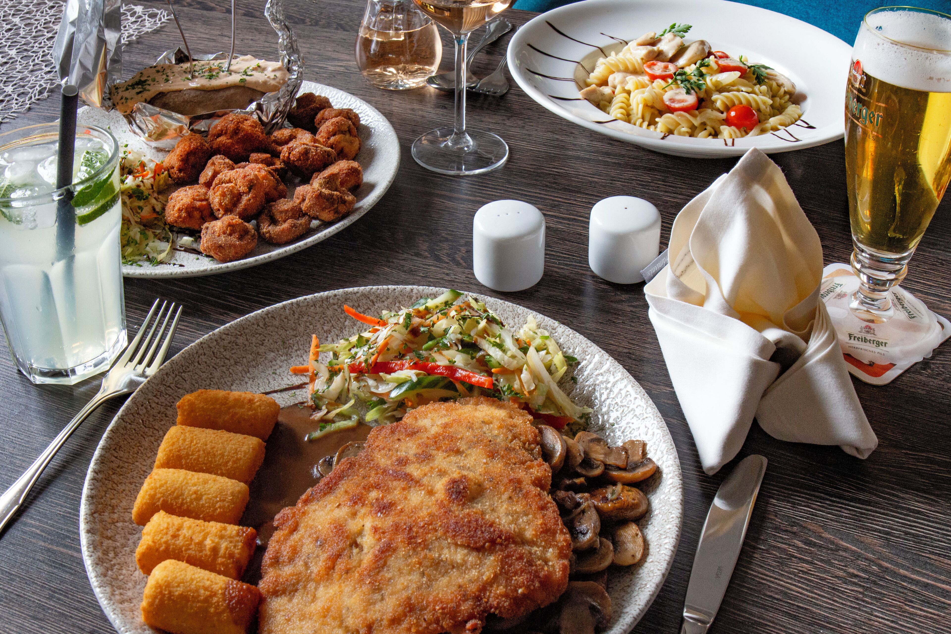 A dining table with various dishes, including fried chicken, pasta, and a glass of beer.