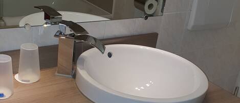 Un baño moderno con un lavabo redondo, un espejo, un perchero para toallas y un inodoro.