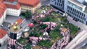 An aerial view of a pink and white building complex with multiple domed structures, surrounded by greenery and adjacent to a road with a tram line.