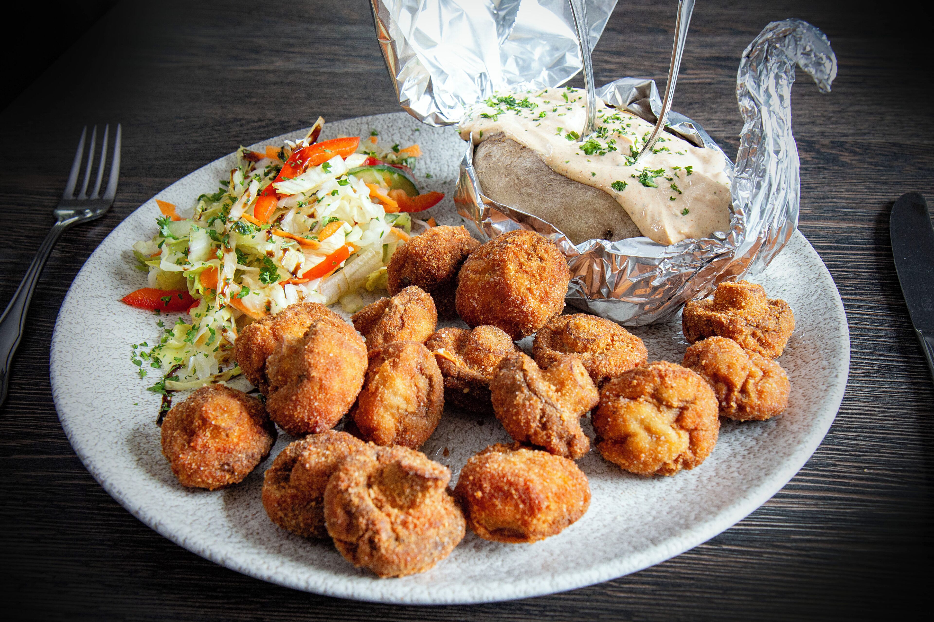 A plate with breaded and fried food, a salad, and a covered dish on a table.