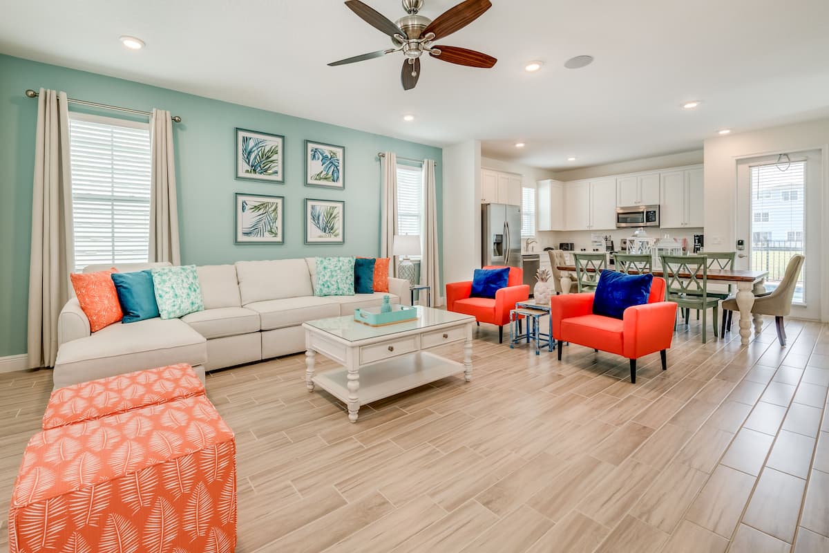 A modern living room with a sofa, coffee table, and two armchairs. There is a dining area with a table and chairs, and a kitchen in the background.