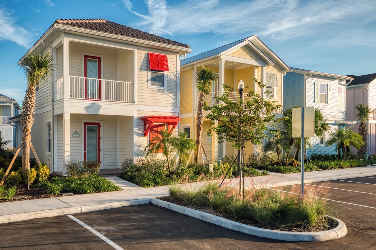 A row of two-story beach houses with balconies, palm trees, and a parking lot.