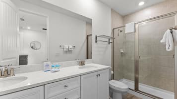 A modern bathroom with two sinks, a large mirror, a glass shower enclosure, and a toilet.