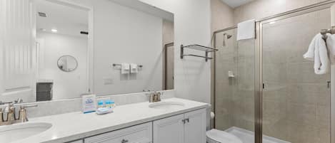 Une salle de bain moderne avec deux lavabos, un grand miroir, une douche à parois de verre et des toilettes.
