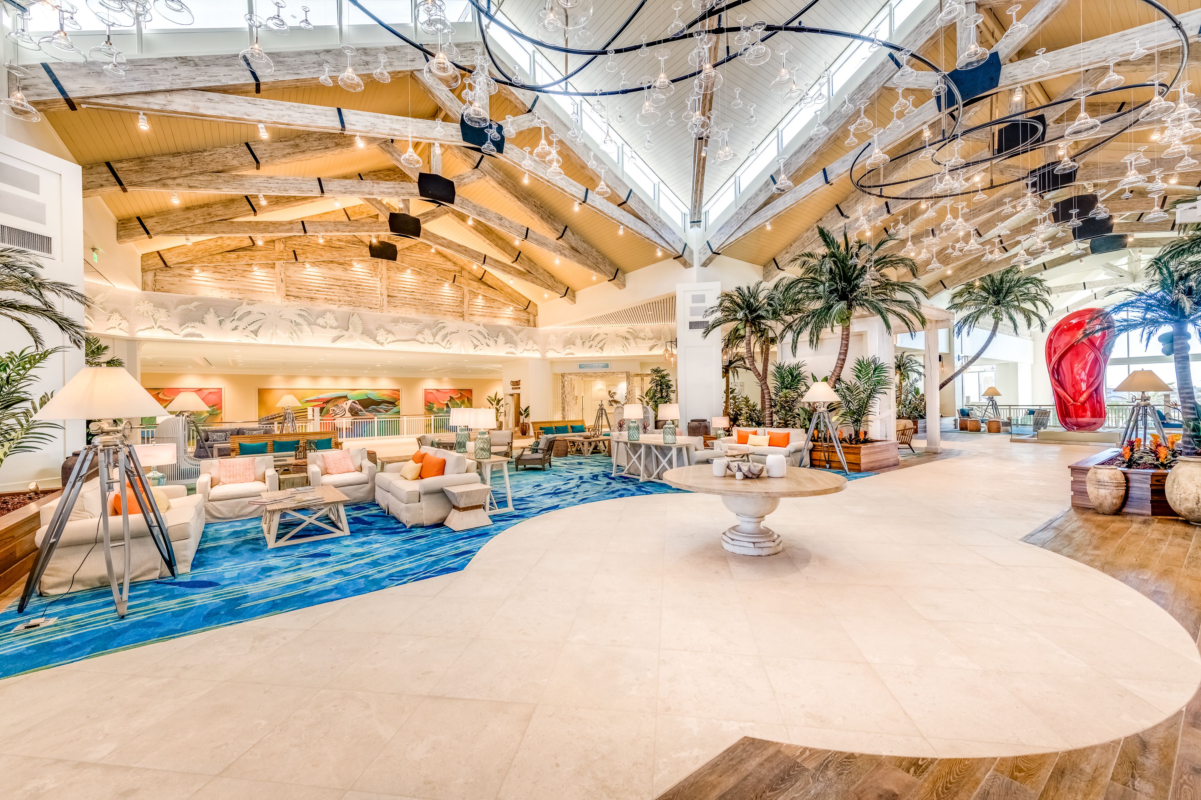 A spacious lobby with a high ceiling, modern lighting fixtures, and a central seating area with sofas and a coffee table.