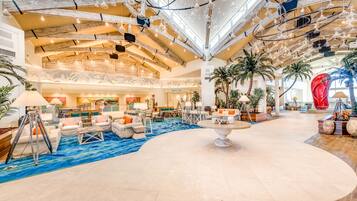A spacious lobby with a high ceiling, modern lighting fixtures, and a central seating area with sofas and a coffee table.