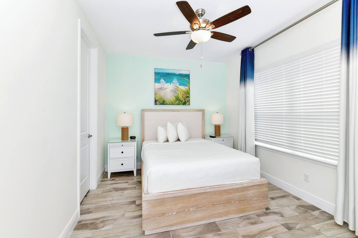 A bedroom with a bed, nightstands, a ceiling fan, and a painting on the wall.