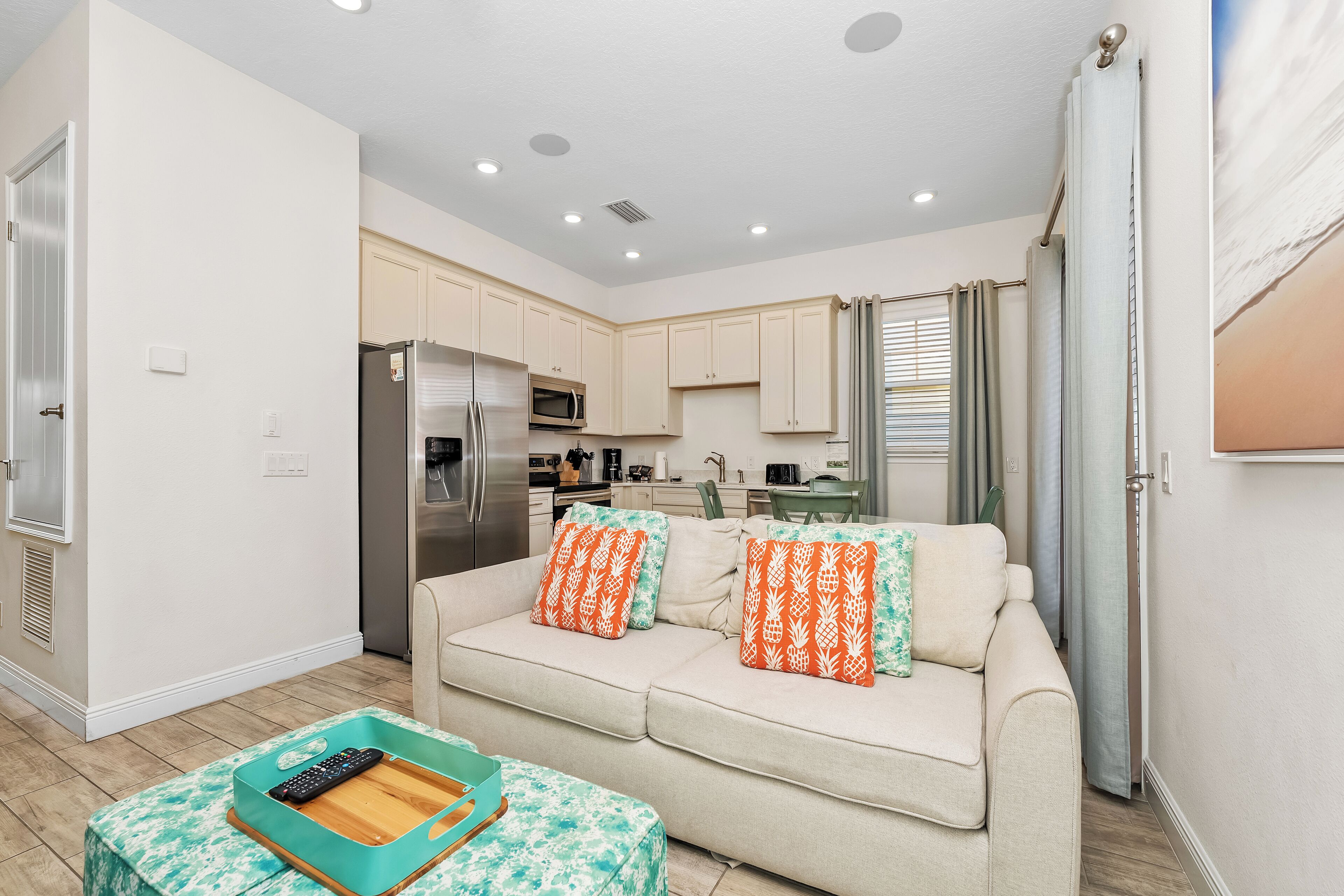Un espacio habitable compacto con kitchenette, un sofá con cojines estampados y una mesita con bandeja y control remoto.