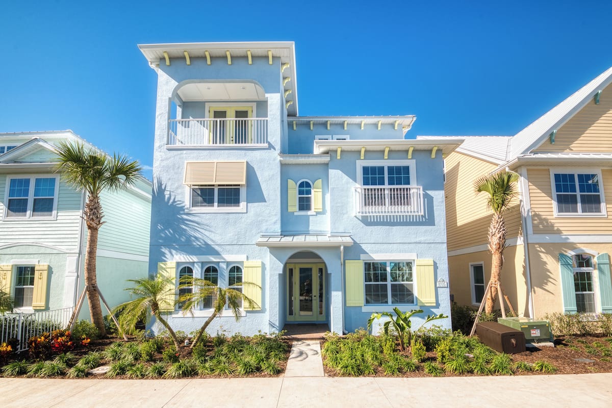 A two-story house with a front porch, a balcony, and a small garden with palm trees.