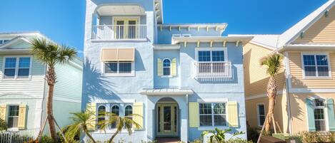 A two-story house with a front porch, a balcony, and a small garden with palm trees.