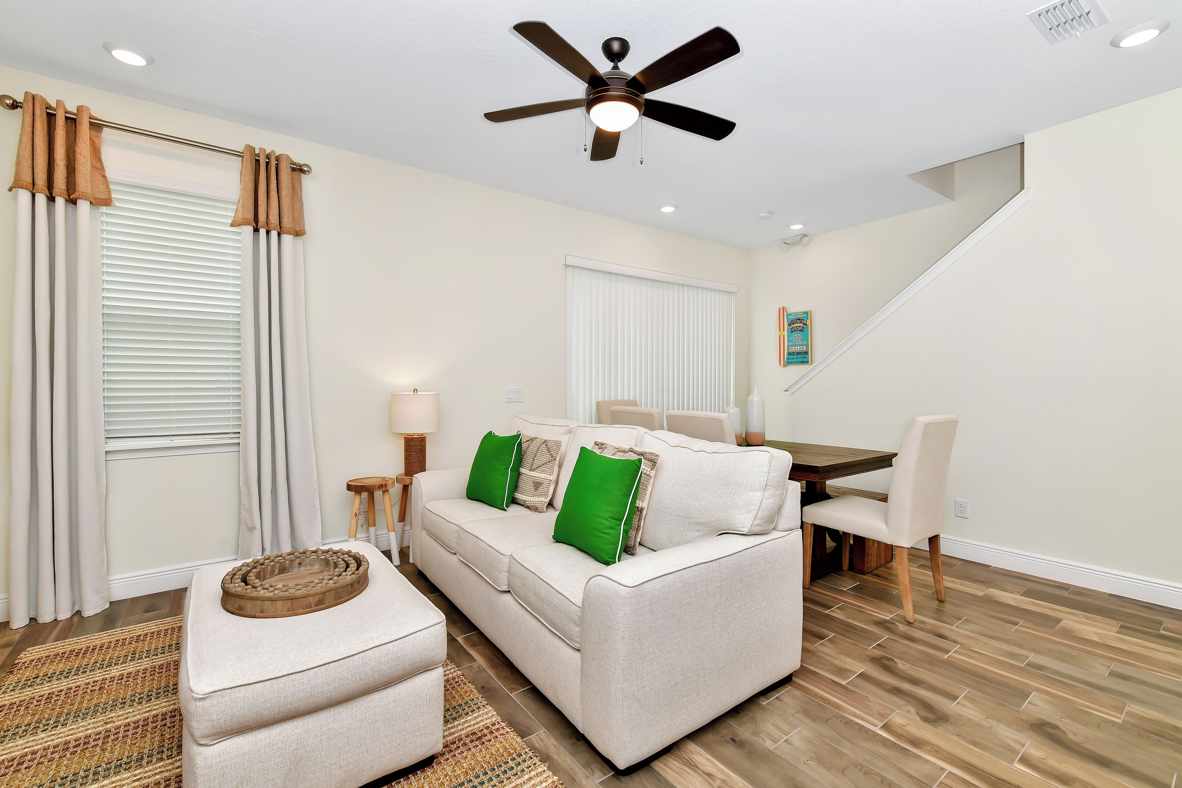 A living room with a sofa, ottoman, and a ceiling fan.