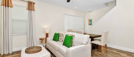 A living room with a sofa, ottoman, and a ceiling fan.
