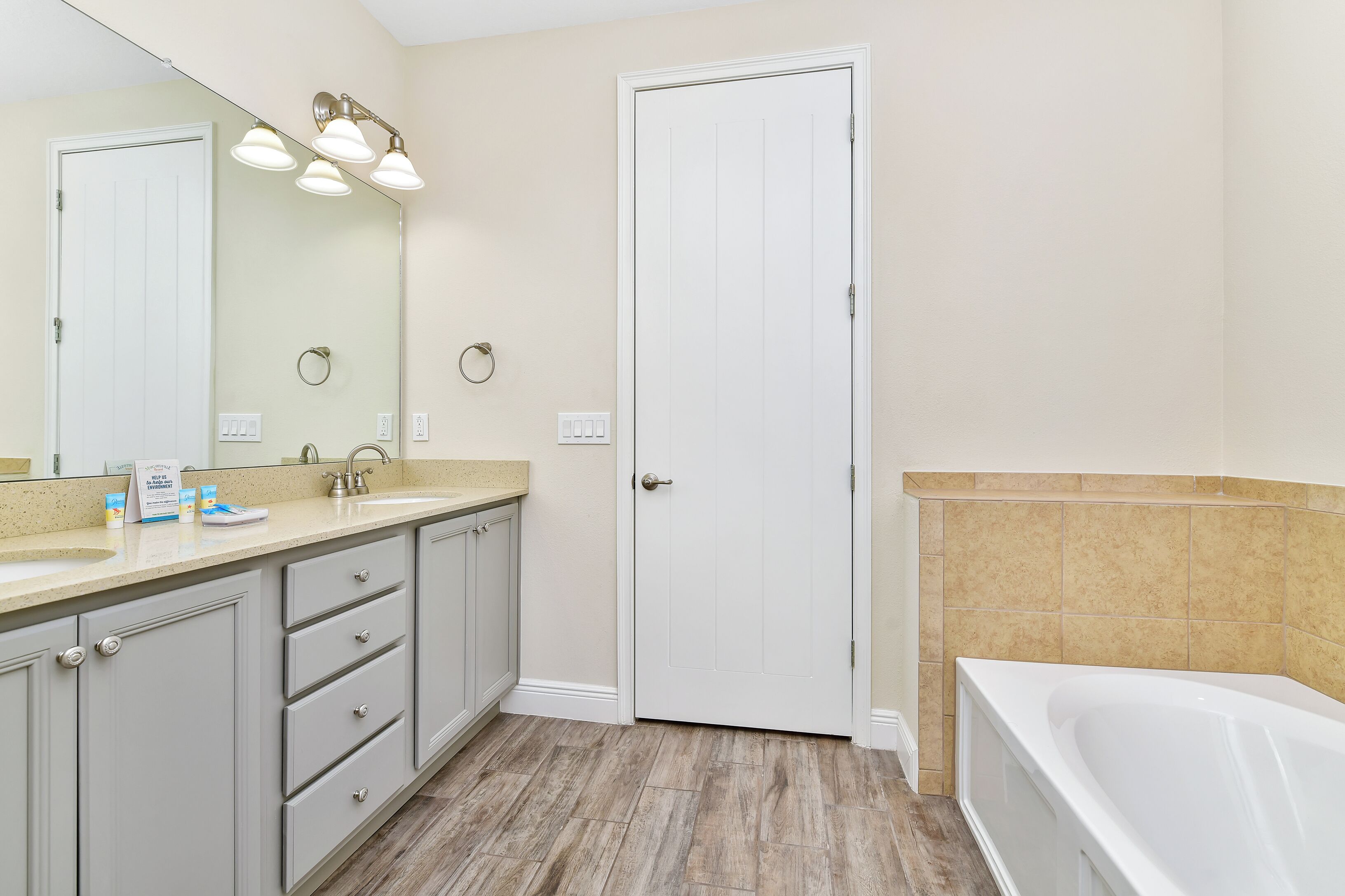 A bathroom with a white door, a sink with a mirror, and a bathtub.