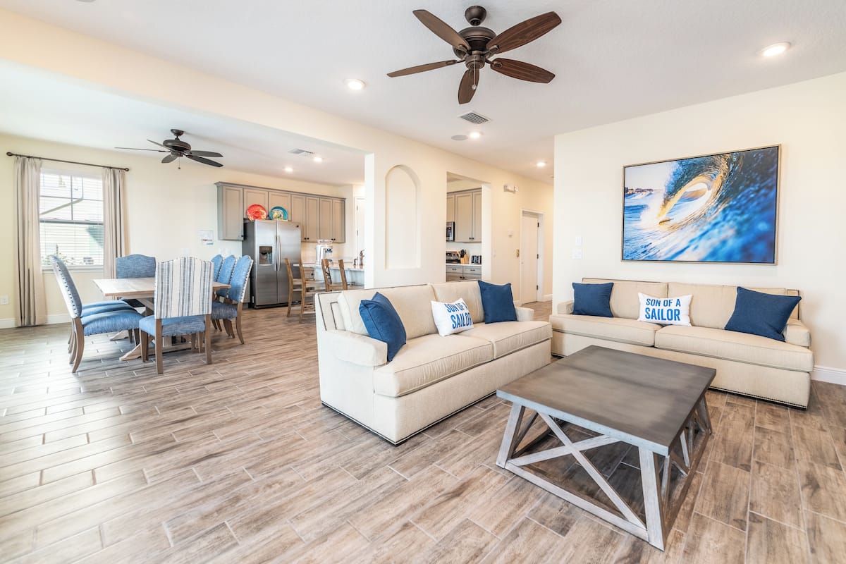 A spacious living room with a beige sofa, two blue pillows, a coffee table, and a ceiling fan.