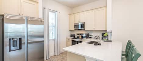 A modern kitchen with stainless steel appliances, a white countertop, and green chairs.