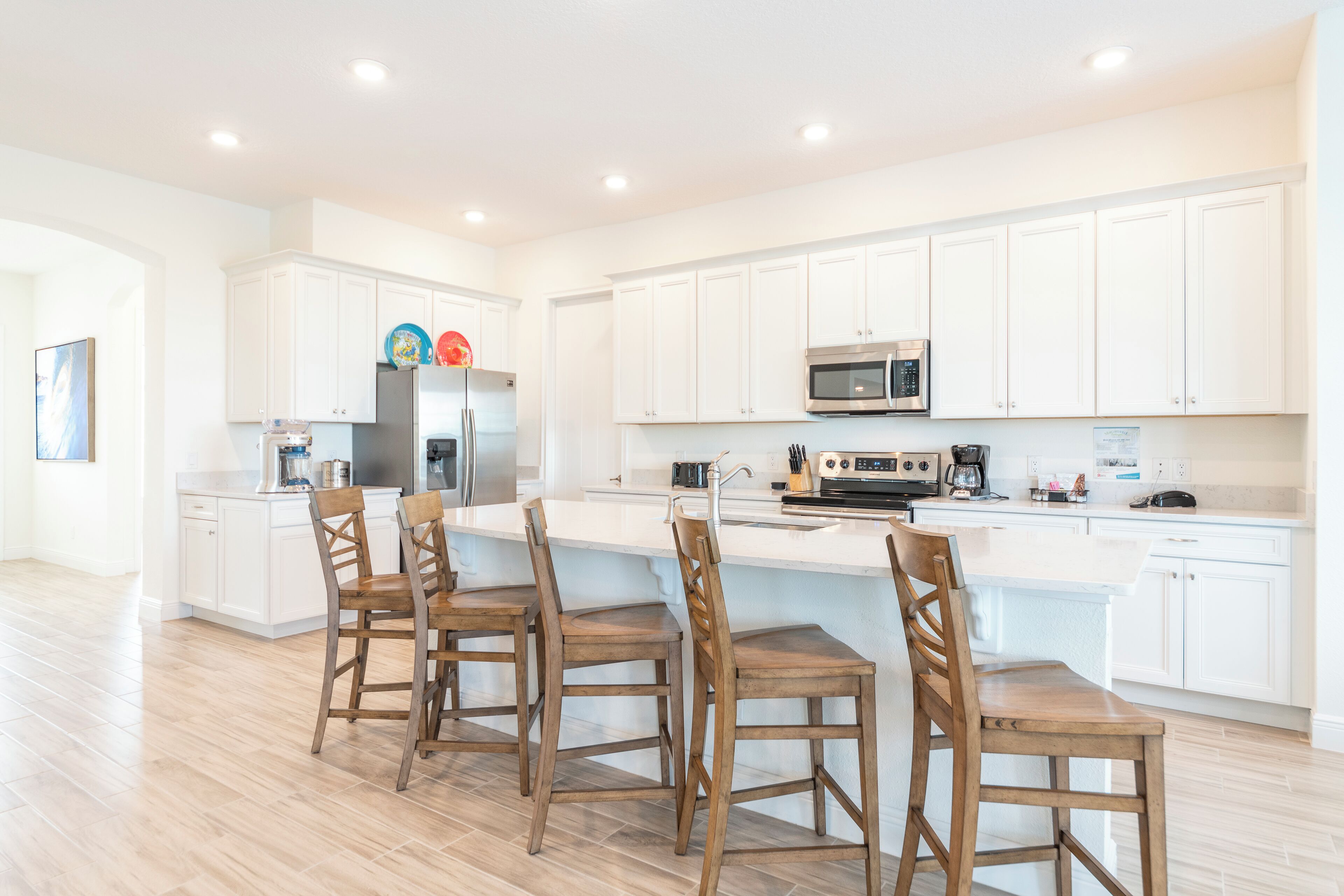 Una cocina moderna con armarios blancos, una isla central con taburetes altos y electrodomésticos de acero inoxidable.