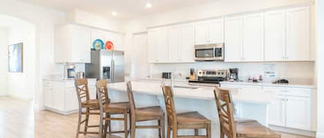 A modern kitchen with white cabinets, a central island with bar stools, and stainless steel appliances.