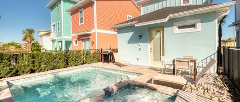 A swimming pool with a hot tub, surrounded by colorful houses and a wooden deck.