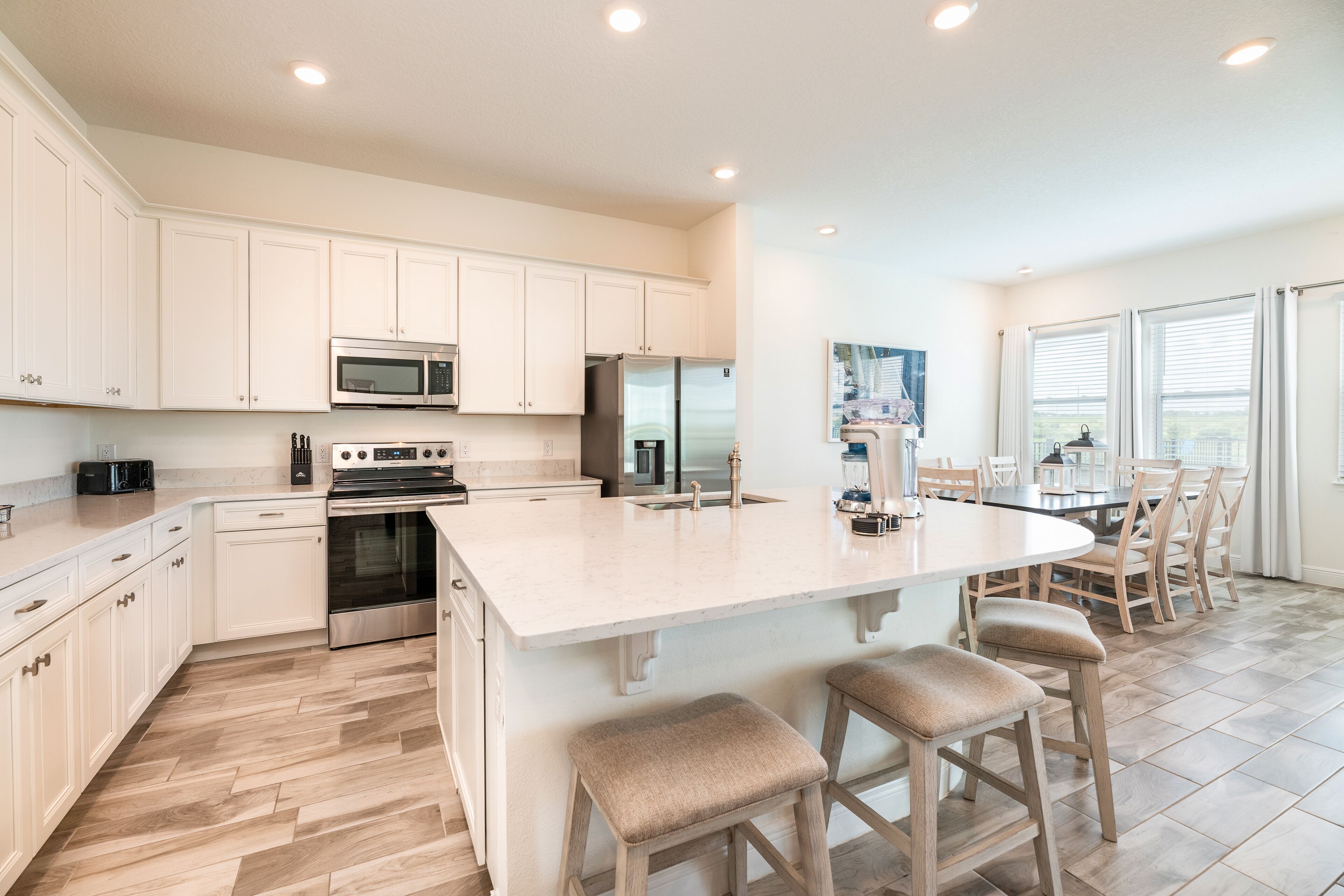 A modern kitchen with white cabinetry, stainless steel appliances, and a large island with bar stools.