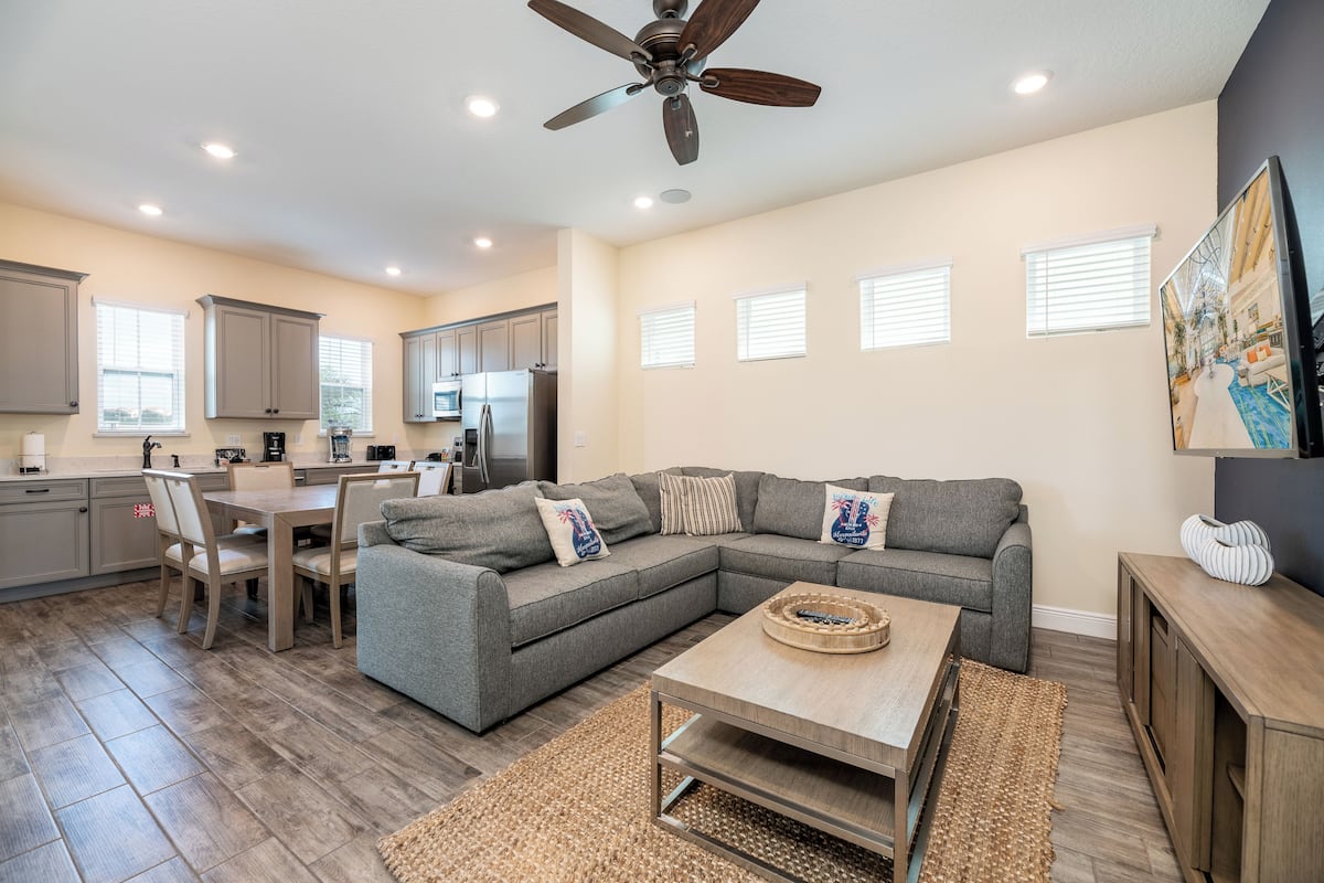 A modern kitchen with a dining area, a gray sectional sofa, and a ceiling fan.