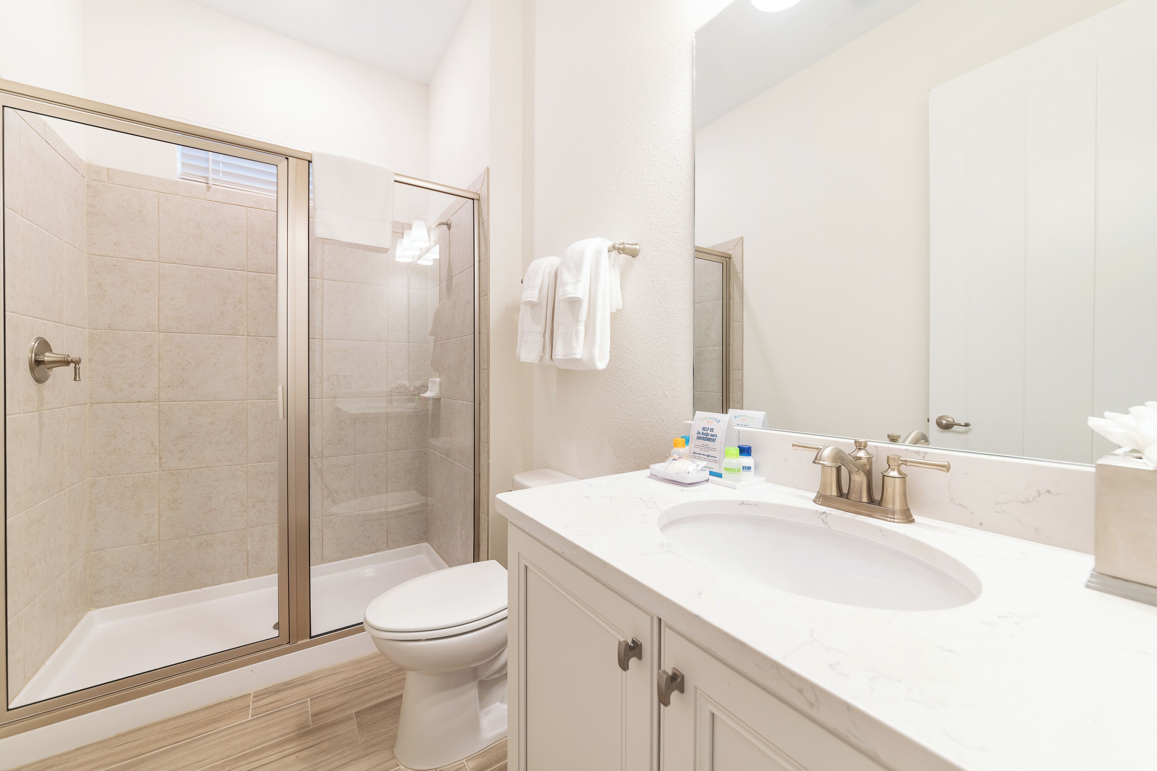A modern bathroom with a glass-enclosed shower, a white toilet, and a vanity with a sink and mirror.