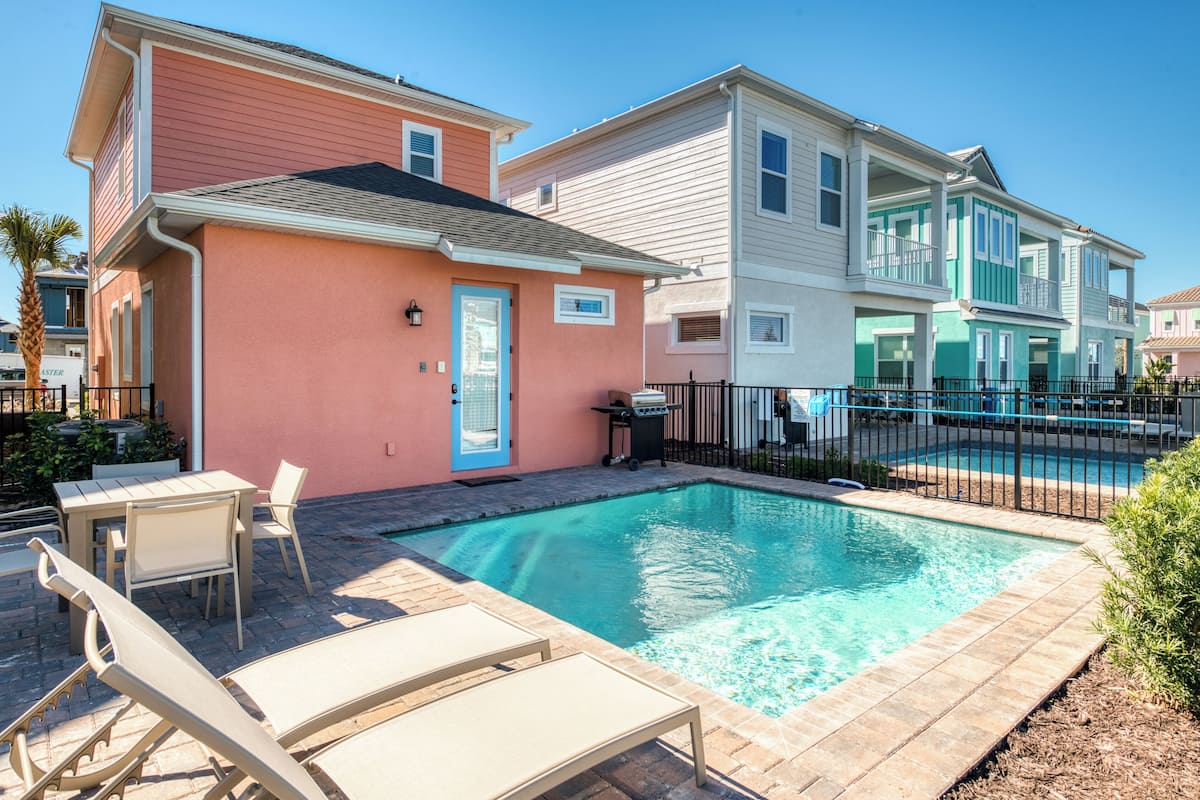 A residential property with a swimming pool, a patio with lounge chairs, and a two-story building with a balcony.