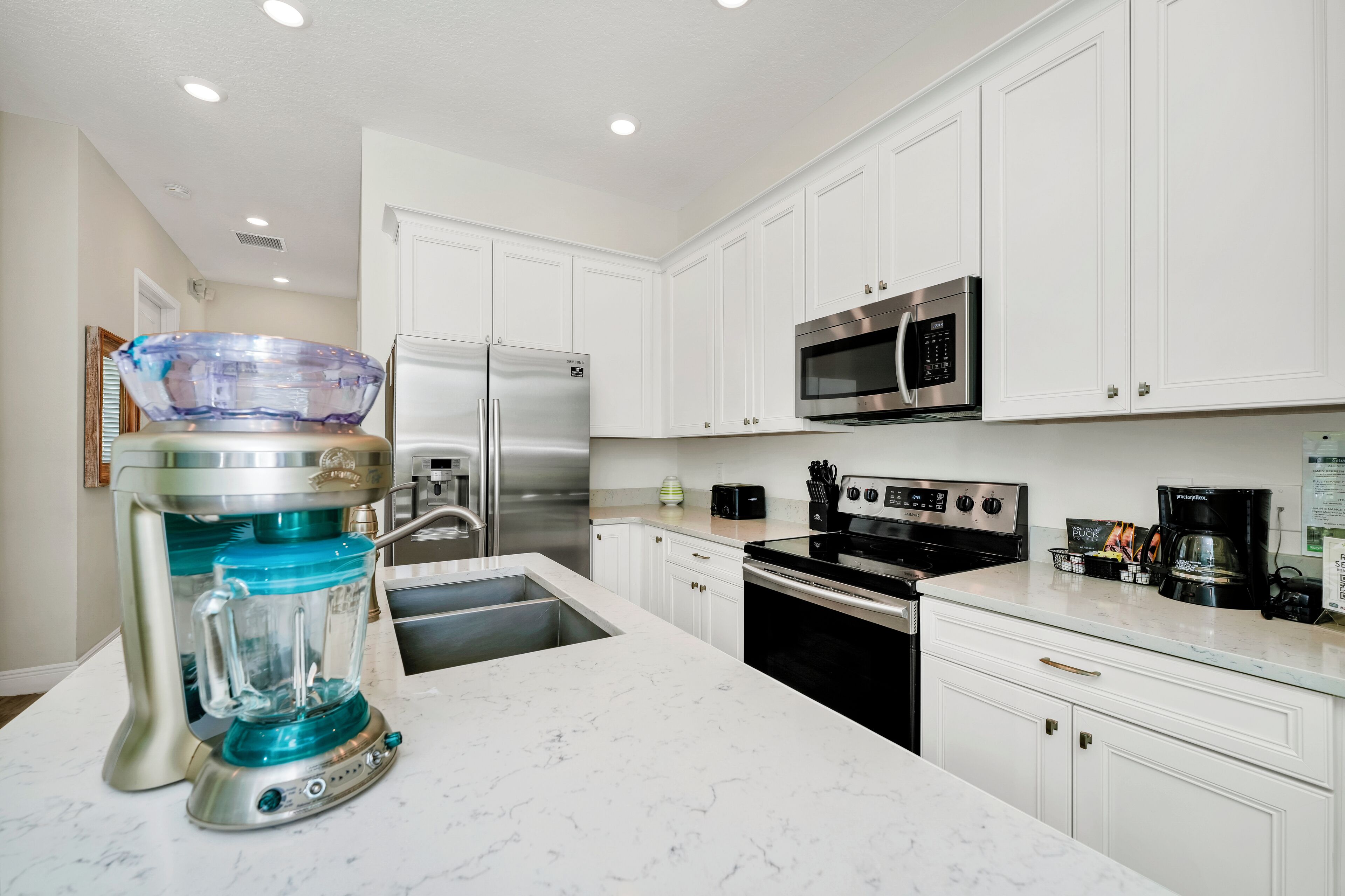 A modern kitchen with white cabinets, stainless steel appliances, and a marble countertop.
