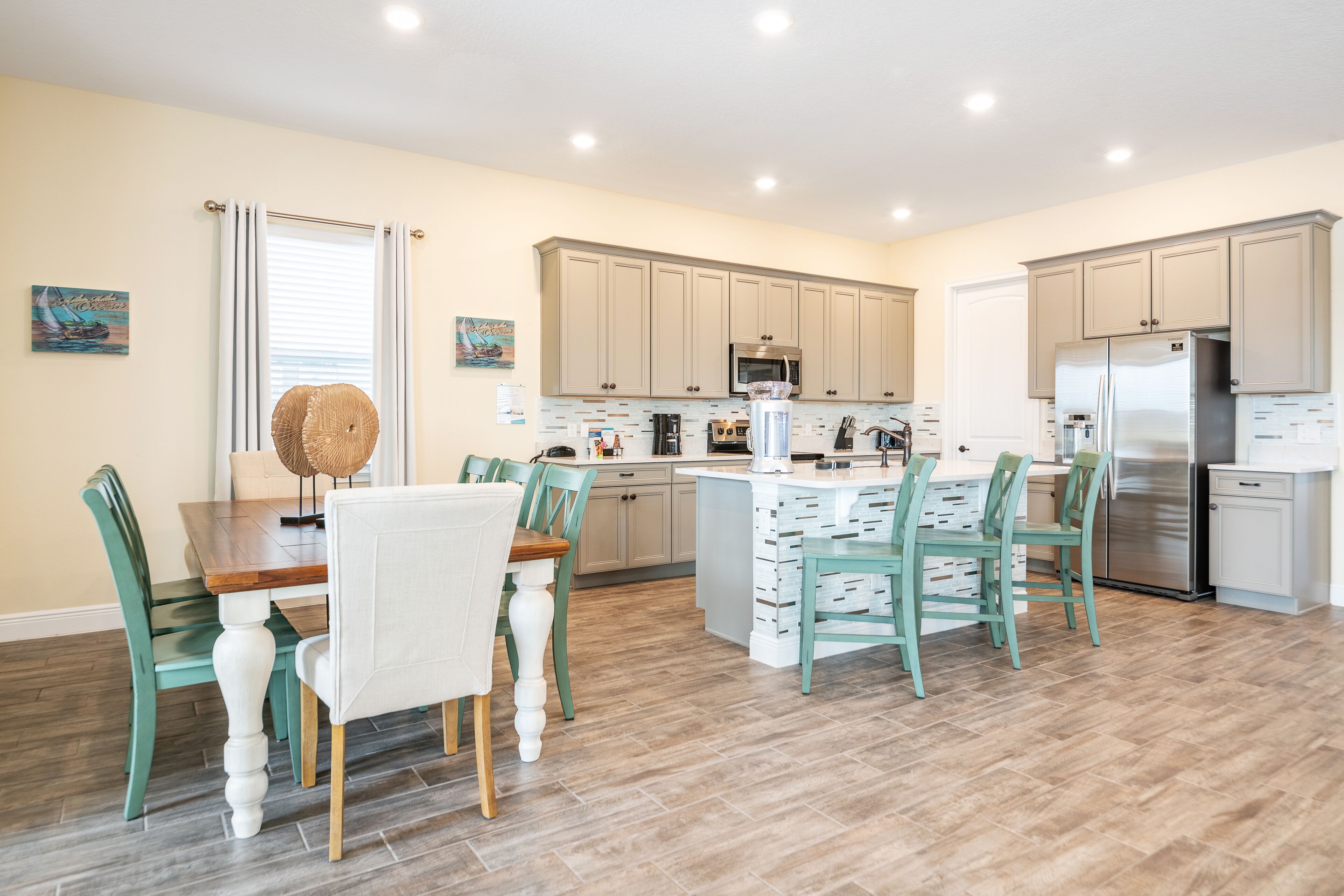 Una cocina moderna con armarios de madera clara, una isla central y sillas color turquesa.