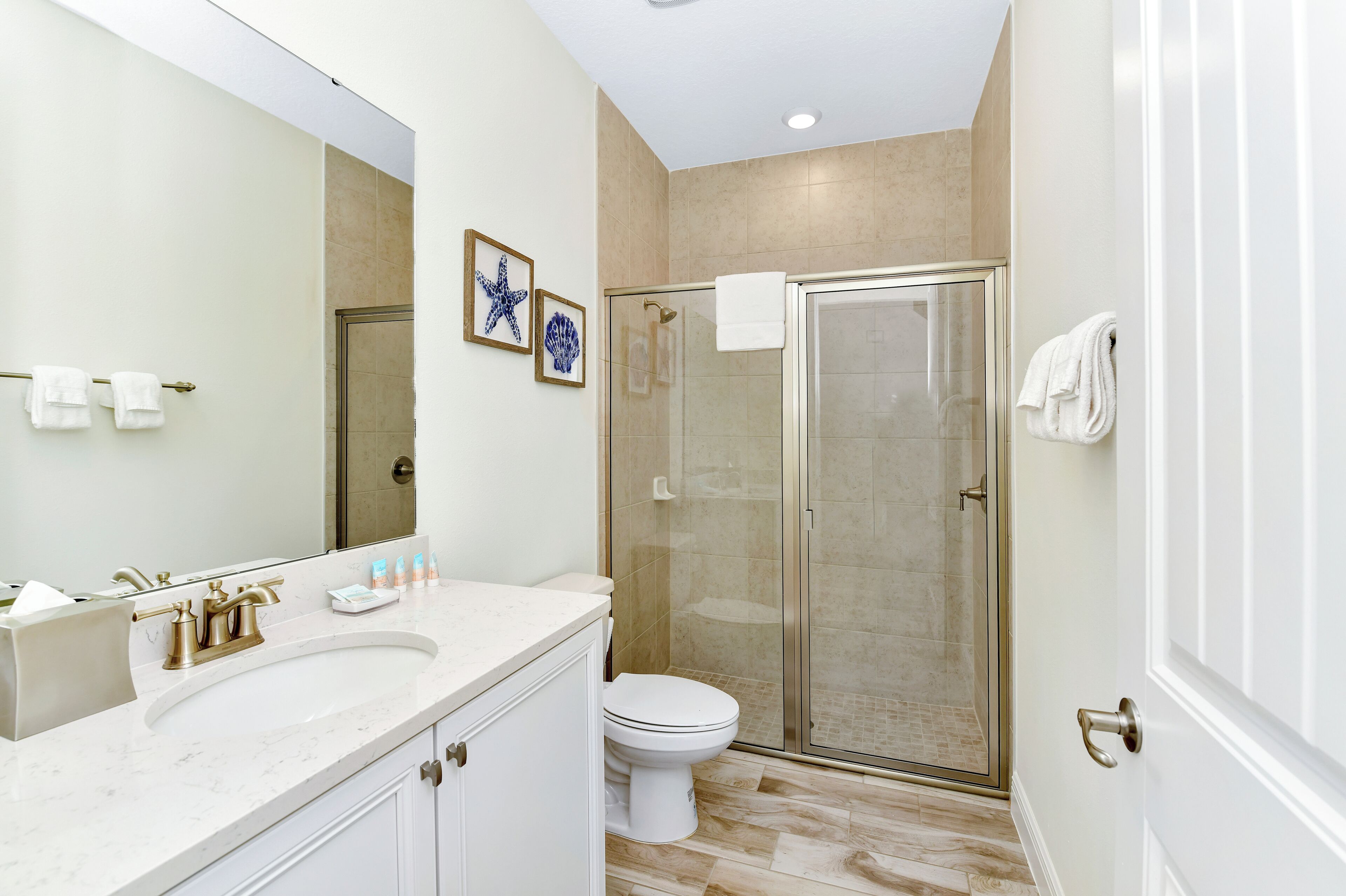 A bathroom with a white sink, a toilet, a glass shower enclosure, and a large mirror.