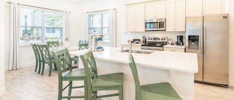 A modern kitchen with white cabinets, stainless steel appliances, and a central island with bar stools.