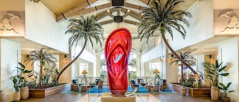 A spacious lobby with a large red sculpture, wooden ceiling beams, and multiple palm trees.