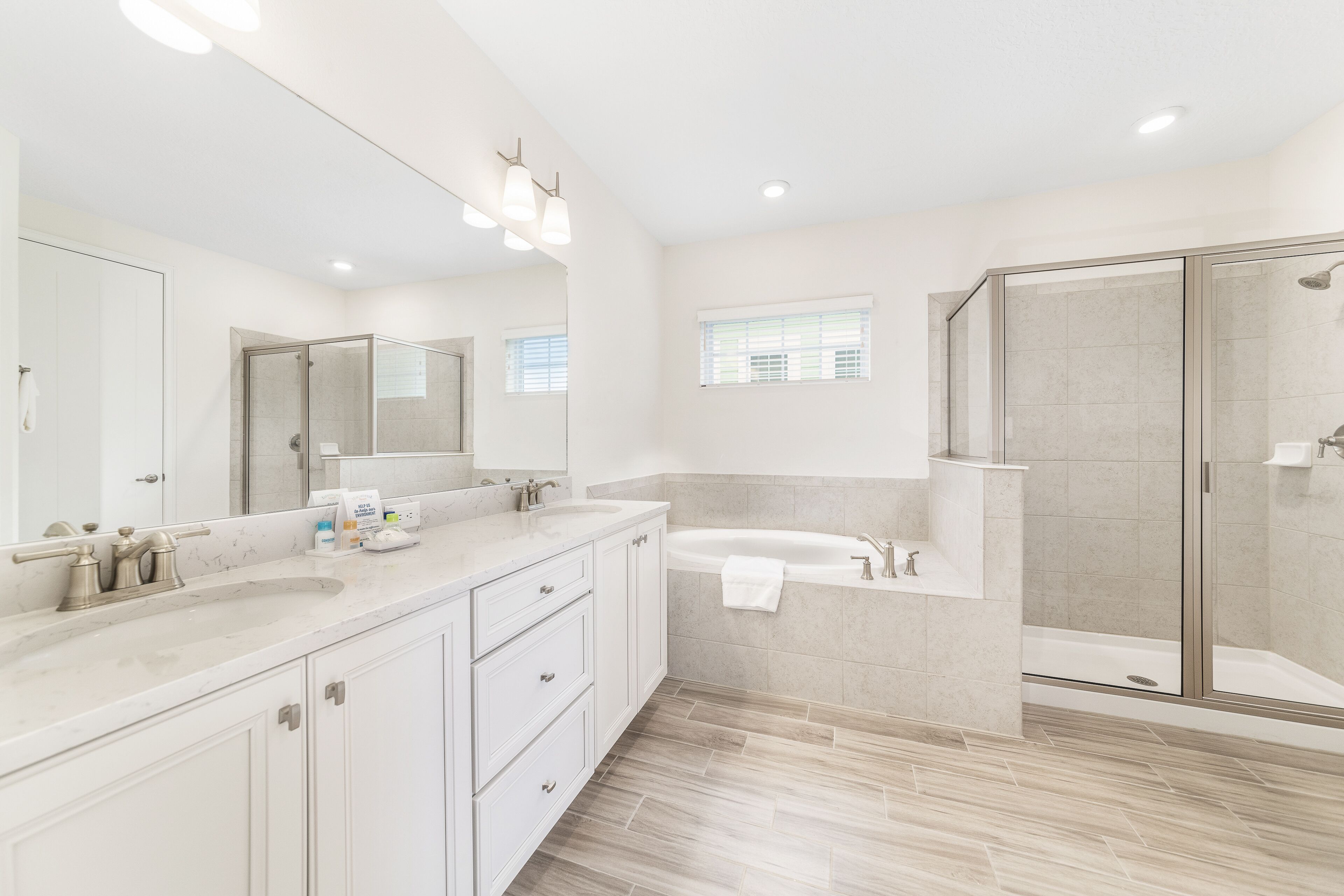Un bagno moderno con uno specchio grande, due lavandini, una vasca e una doccia a filo pavimento.