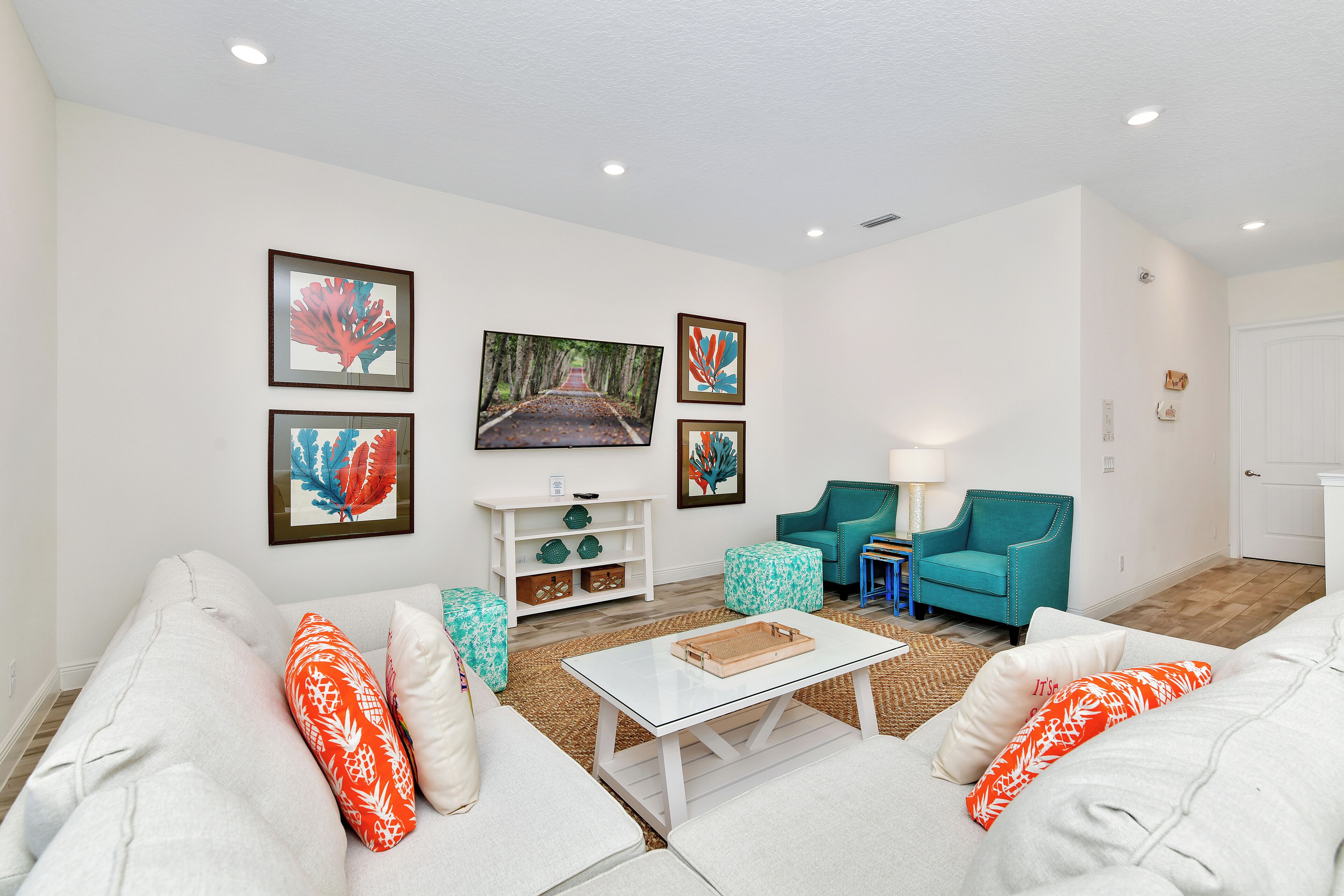 A living room with white sofas, a glass coffee table, teal armchairs, and framed artwork on the walls.