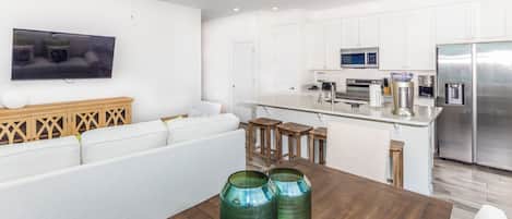 Une cuisine moderne avec des meubles blancs, un réfrigérateur en acier inoxydable et une table à manger en bois agrémentée de deux vases verts.