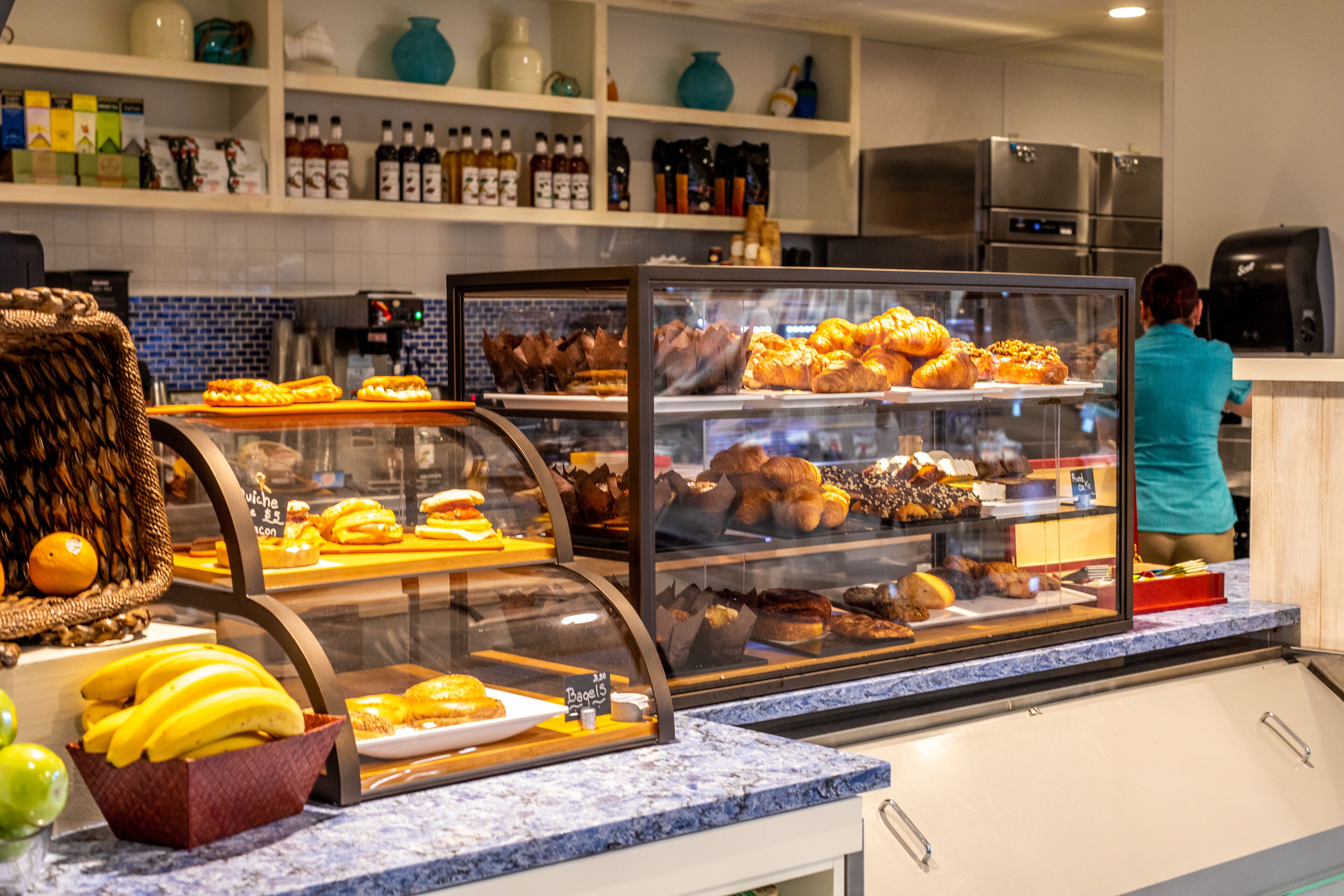Une vitrine de boulangerie où sont exposés divers produits de pâtisserie, ainsi qu’un comptoir avec un panier de bananes.