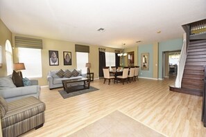 A spacious living room with a grey sofa, a striped armchair, a coffee table, and a dining area with a table and chairs. - Watersong Resort 112ATCJGI - Six Bedroom House (Davenport)