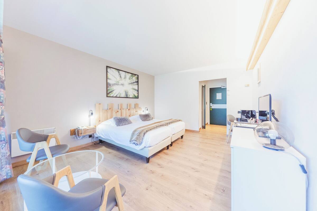 A modern hotel room with a large bed, a desk with a computer, and a chair.