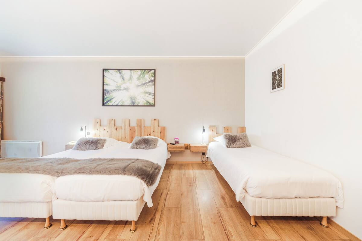 A bedroom with two beds, wooden headboards, a large abstract painting, and a bedside table with a lamp.
