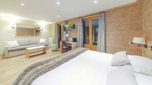A modern hotel room with a wooden accent wall, a large bed, a sofa, a desk, and a TV. - Fleur De Neige Hôtel (Chatel)
