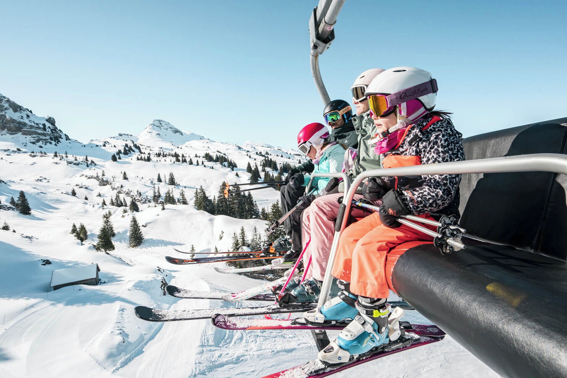 A group of skiers on a ski lift with snow-covered mountains in the background.