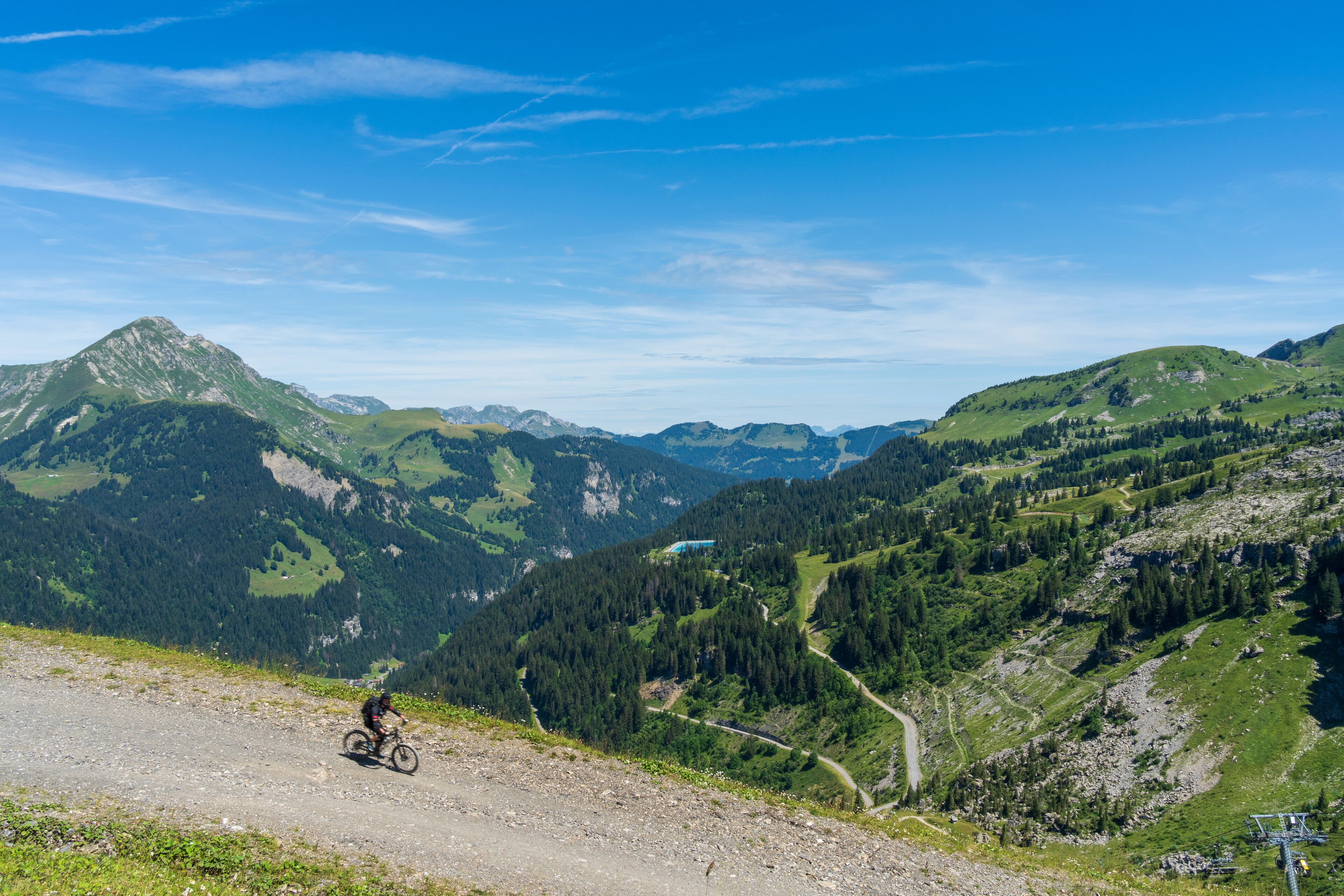 A mountain biker on a dirt path with a view of green hills and a clear sky.