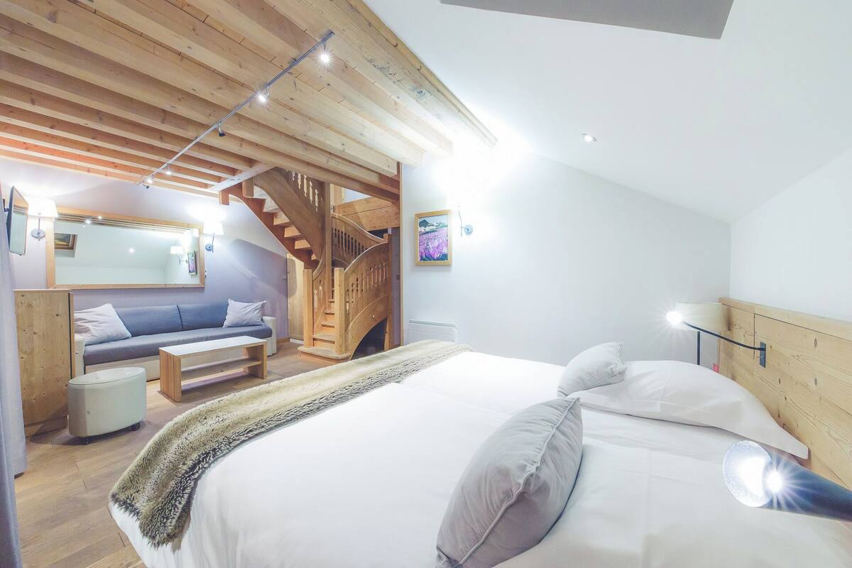 A bedroom with a bed, a wooden staircase, a sofa, and a small table.