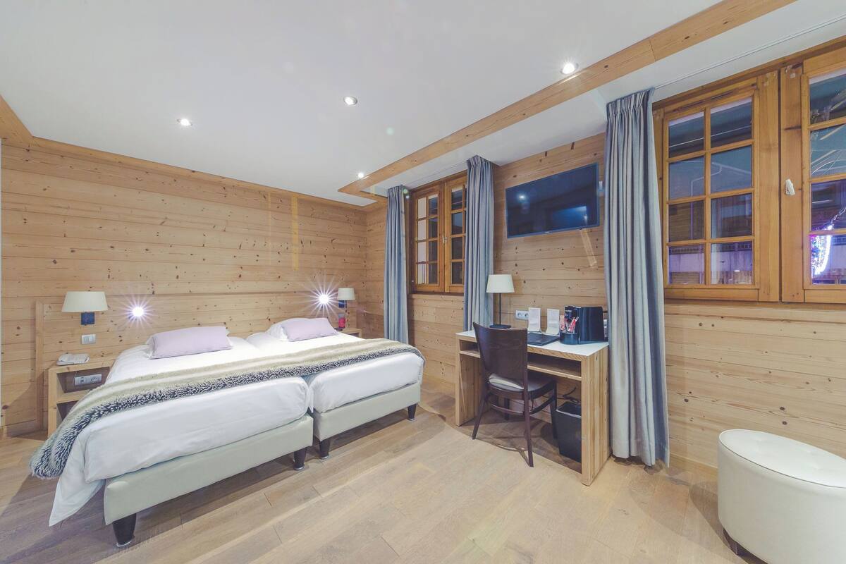 A wooden-paneled room with a bed, desk, chair, and a small white round table.
