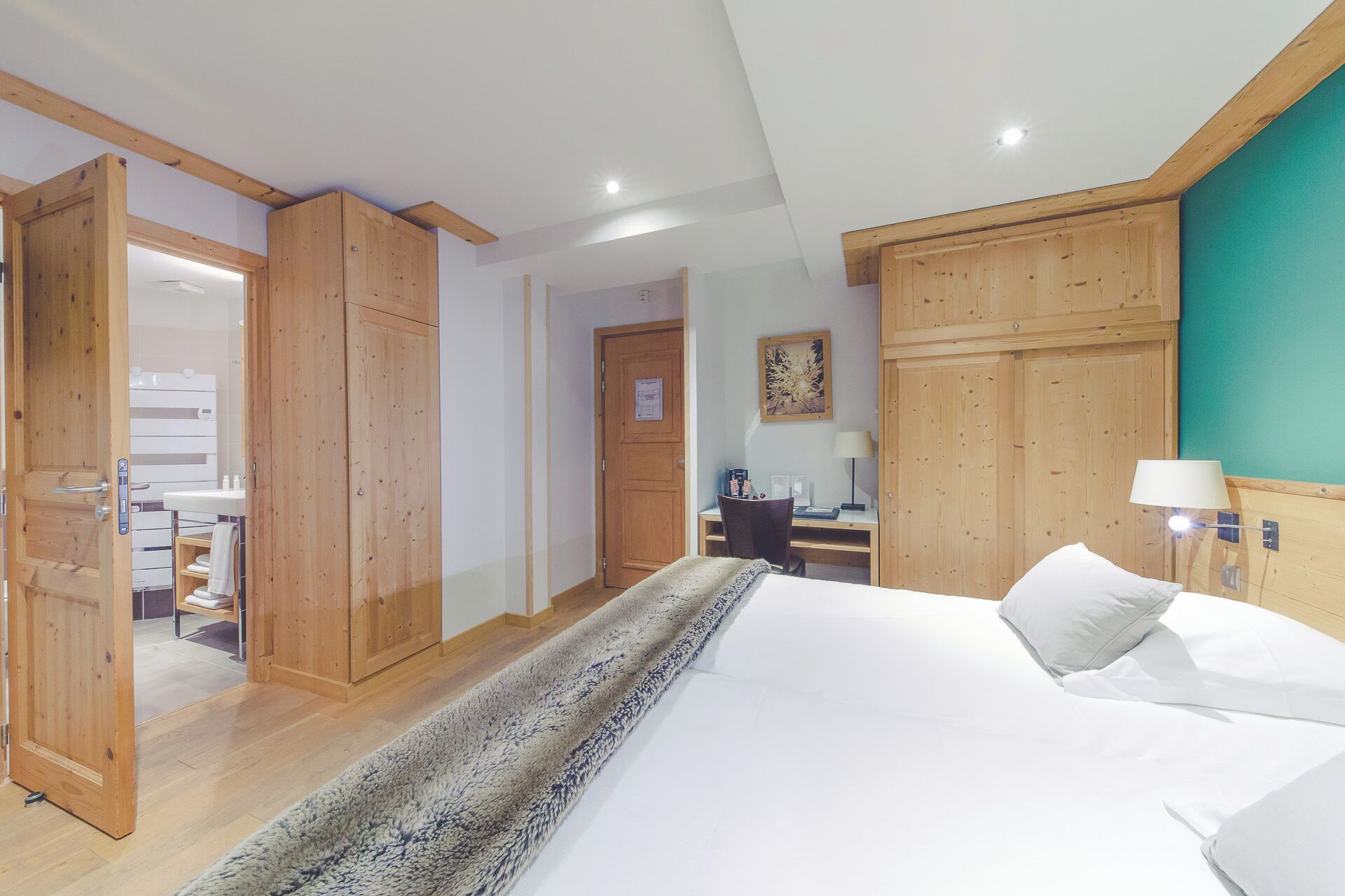 A hotel room with a bed, a desk, a chair, a desk lamp, and wooden paneling on the walls.